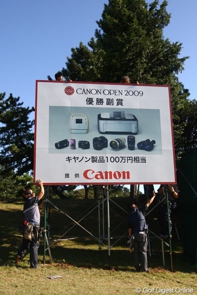 2009年 キヤノンオープン初日 看板 18番ホールに設置されていた優勝副賞の看板も、強風の為に一時取り外されていた。やっと風が収まり再設営。 使用カメラ：Canon EOS-1D Mark Ⅲ