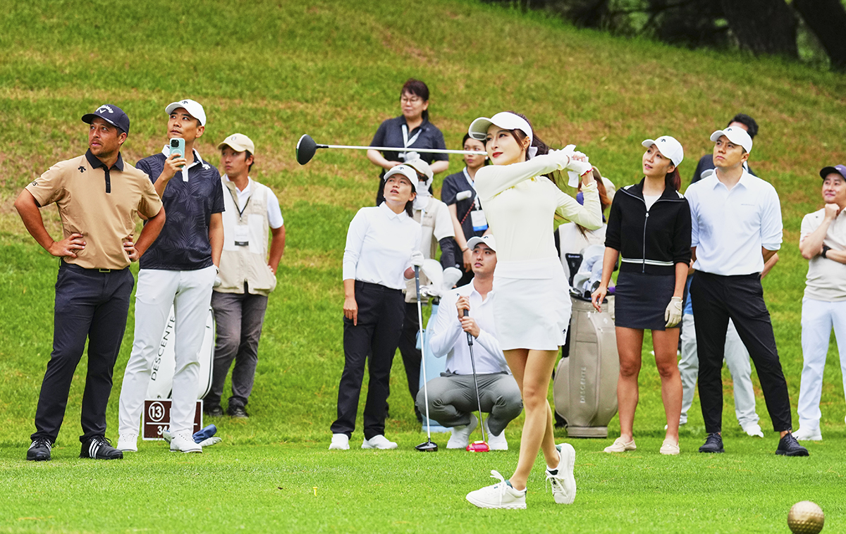 2025年 デサント特集 シャウフェレに見守られてティショットを放つ中国の参加者（デサント提供）